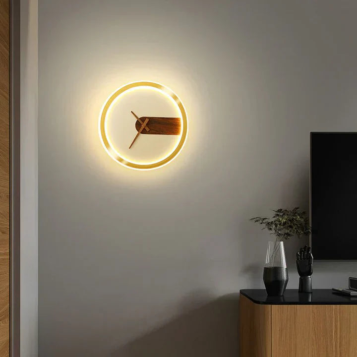 Modern wall clock with neon light on a gray wall in a room with a TV and decor items.