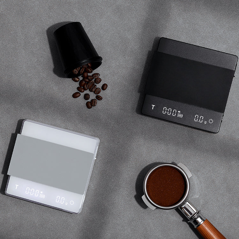 Digital coffee scale with coffee beans and a portafilter on a gray surface