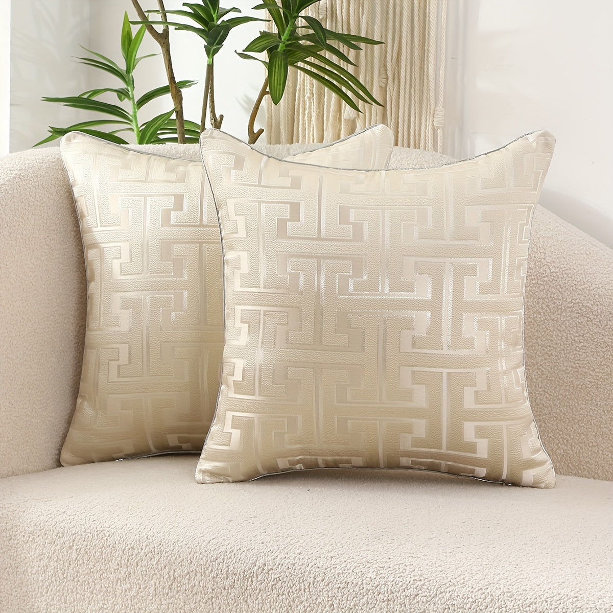Two patterned pillows on a beige sofa with a plant in the background