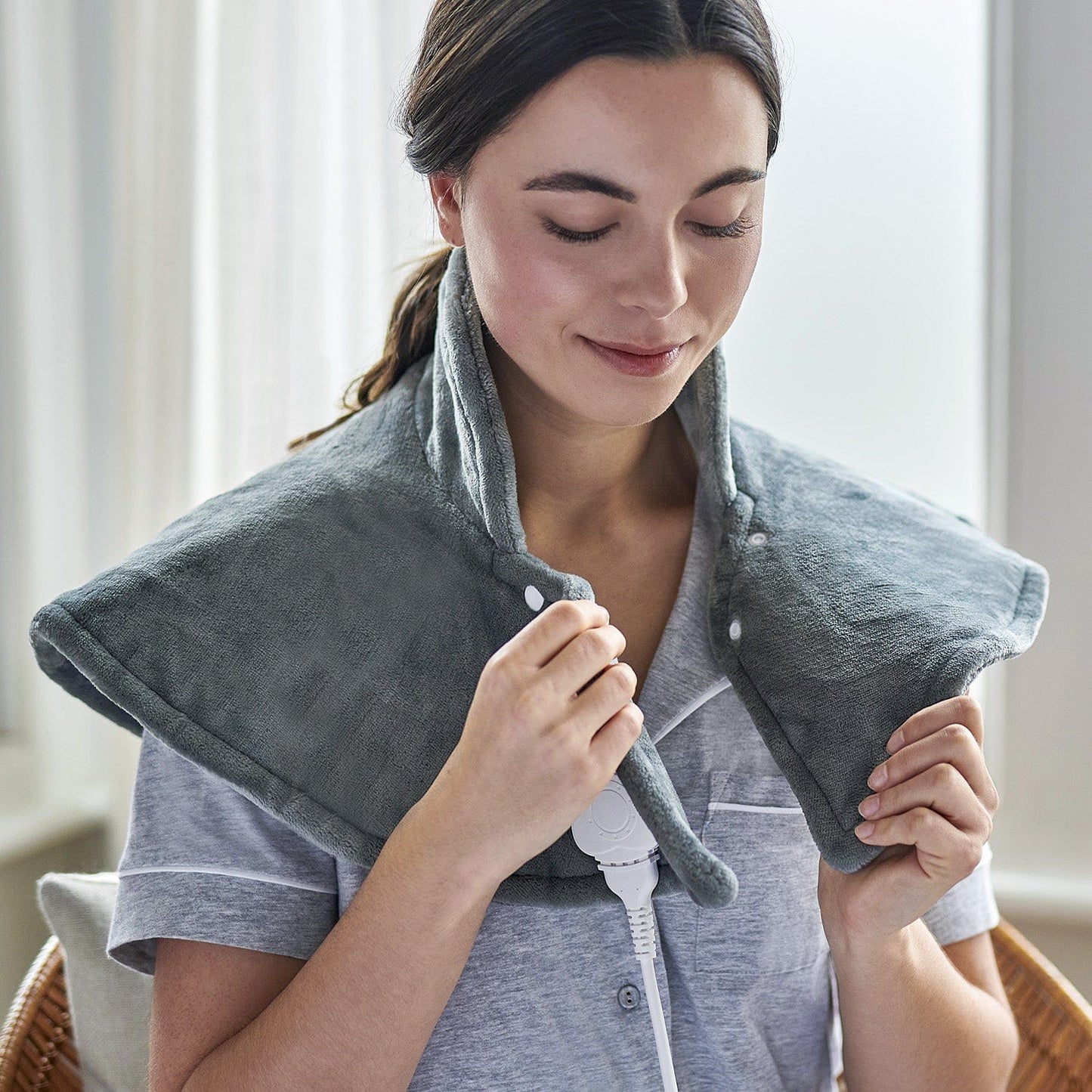 Woman using a gray neck and shoulder massager in a home setting