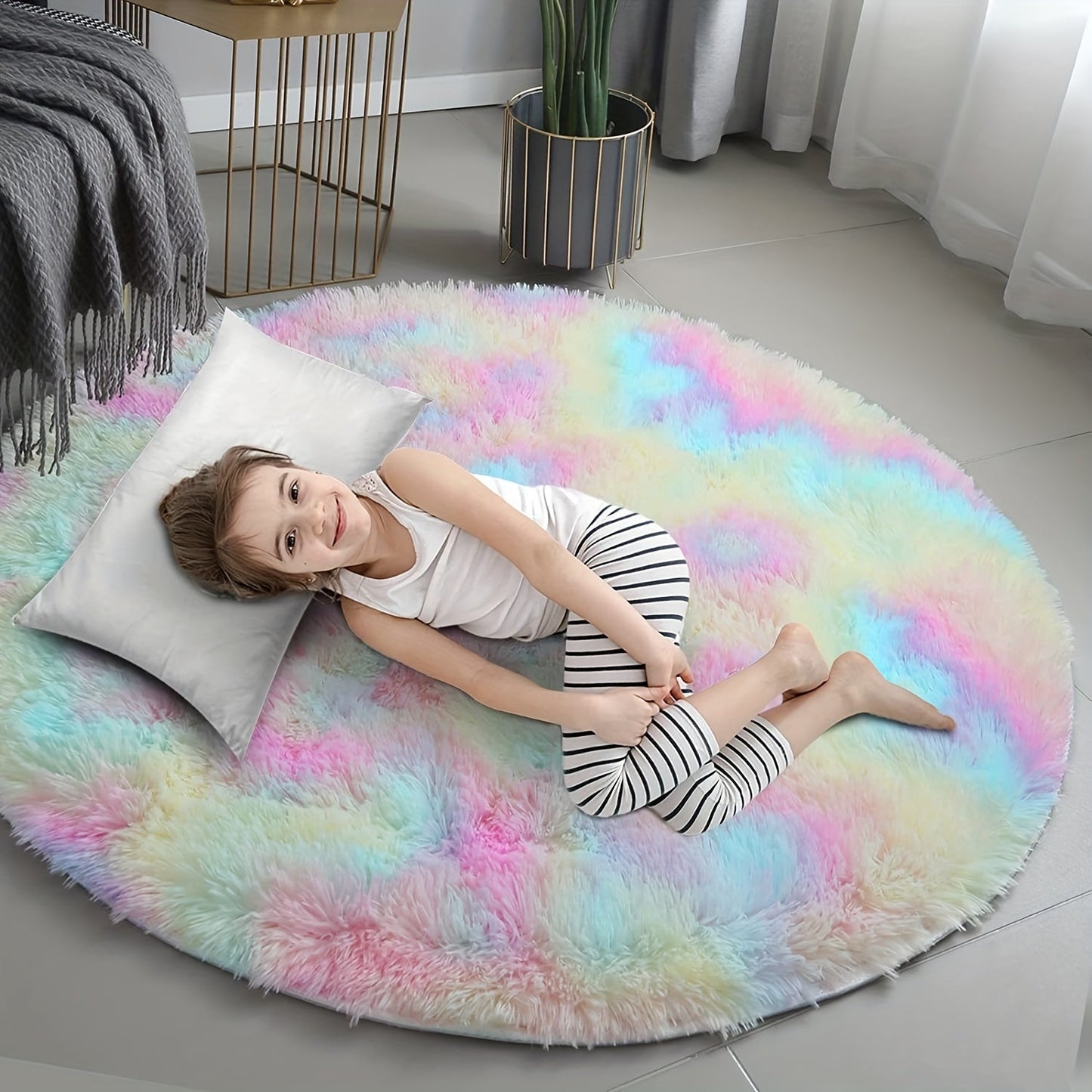 Child lying on a colorful round rug in a room with a plant and table.