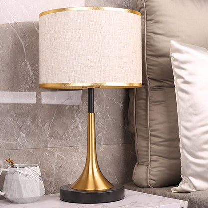 Table lamp with gold base and white shade on a marble surface next to a sofa.