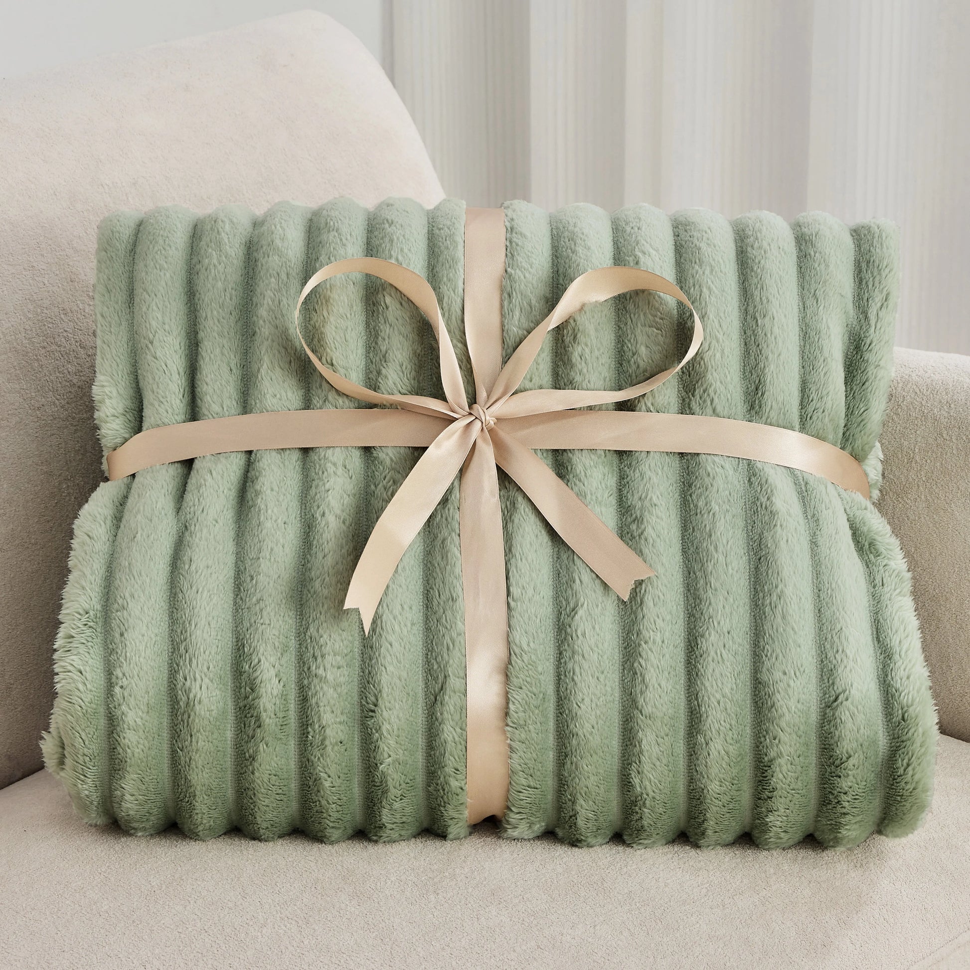 Green plush blanket with a beige ribbon on a light-colored couch.