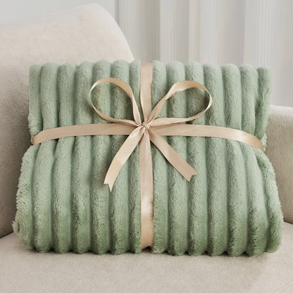 Green plush blanket with a beige ribbon on a light-colored couch.
