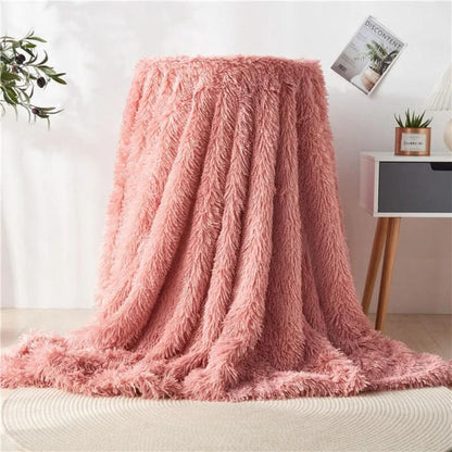 Pink fluffy blanket draped over a chair in a room with a plant and magazine in the background.
