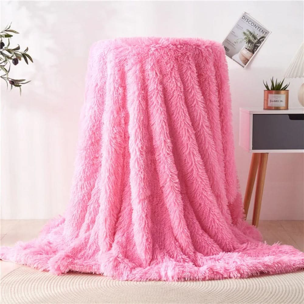 Pink fluffy blanket draped over a chair in a room with a plant and TV in the background.