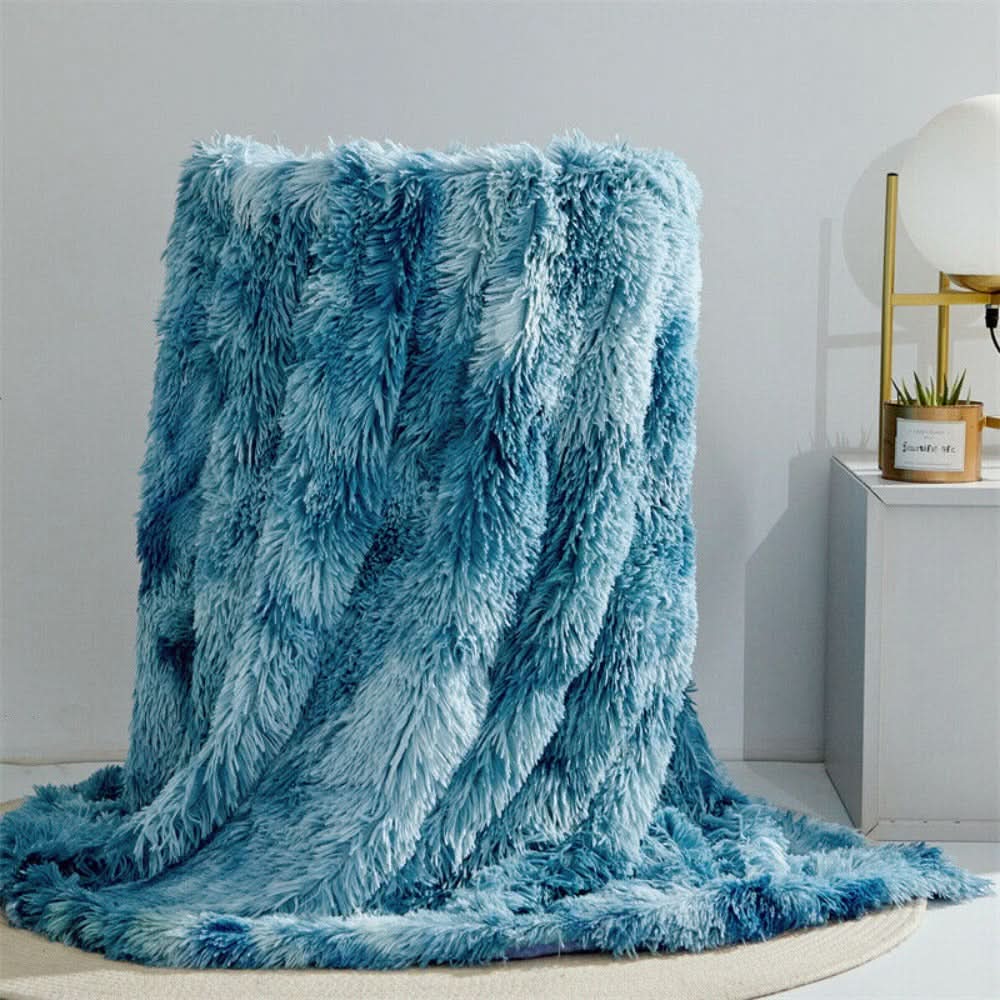 Blue fluffy blanket draped over a chair in a room with a white wall and small table.