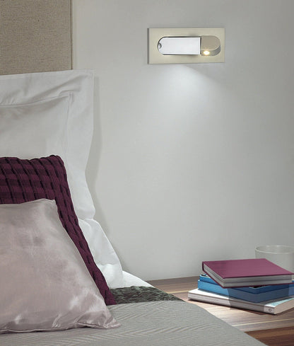 Bedroom setting with a wall-mounted light fixture, books, and pillows.