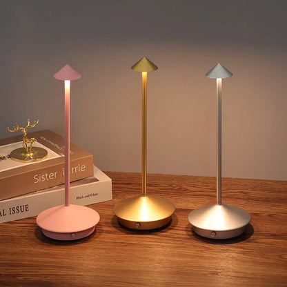 Three colorful desk lamps on a wooden surface with books in the background.