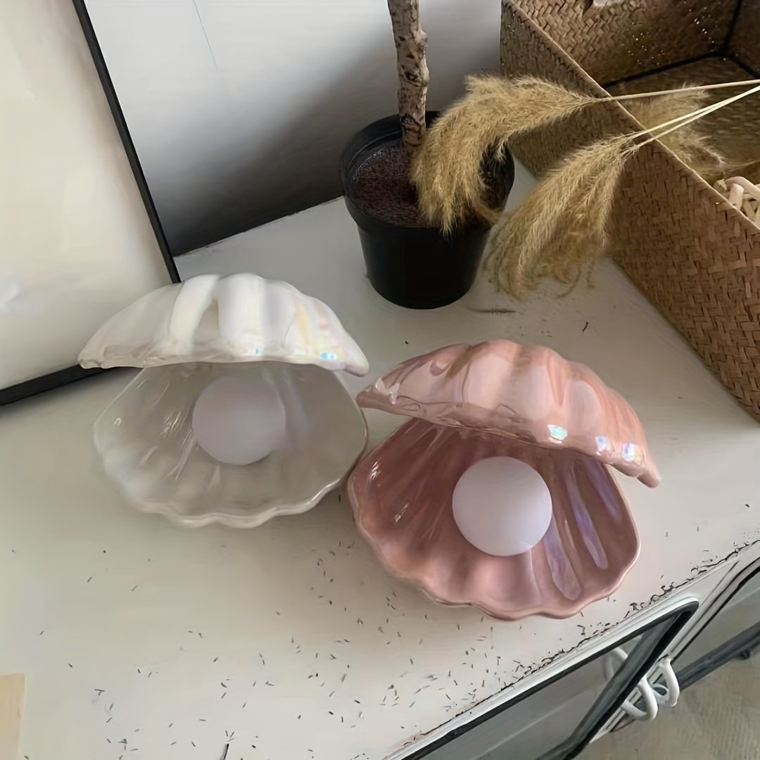 Two shell-shaped candle holders on a surface with a plant in the background.