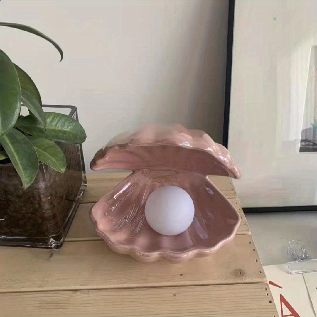 Pink shell with a white ball inside on a wooden surface next to a plant.