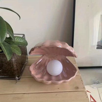 Pink shell with a white ball inside on a wooden surface next to a plant.