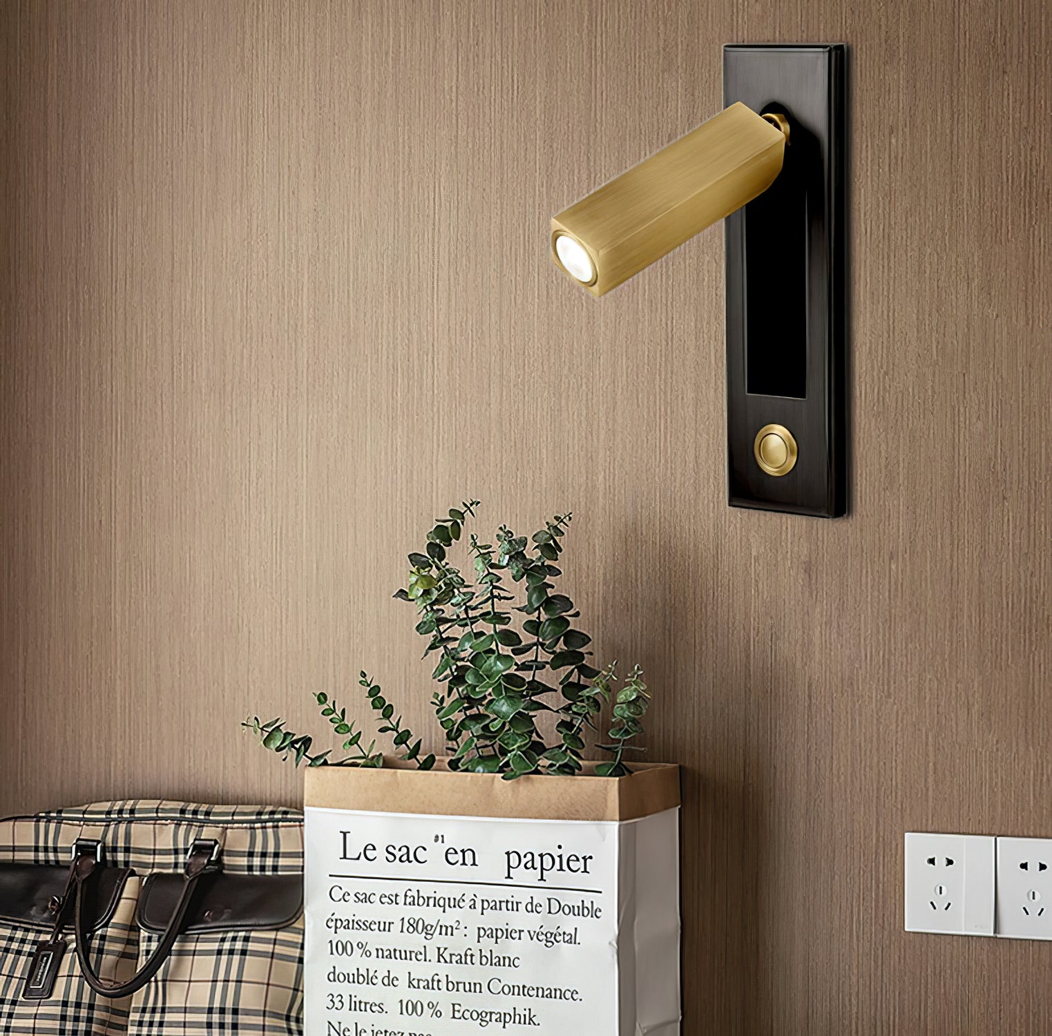 Decorative wall light fixture on a wooden wall with a plant and suitcase in the foreground.