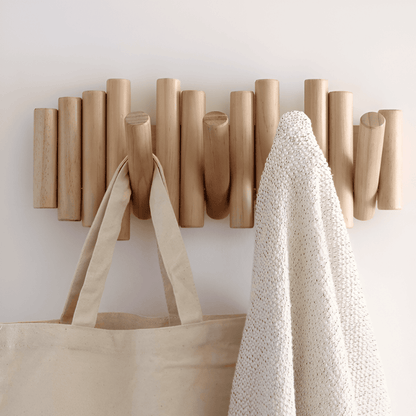 Wooden wall hook with a beige tote bag and white textured garment on a light gray background