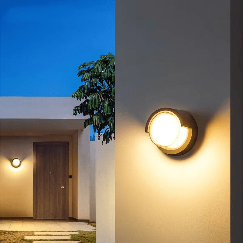 Outdoor wall lights illuminating a pathway and door area with a clear blue sky.