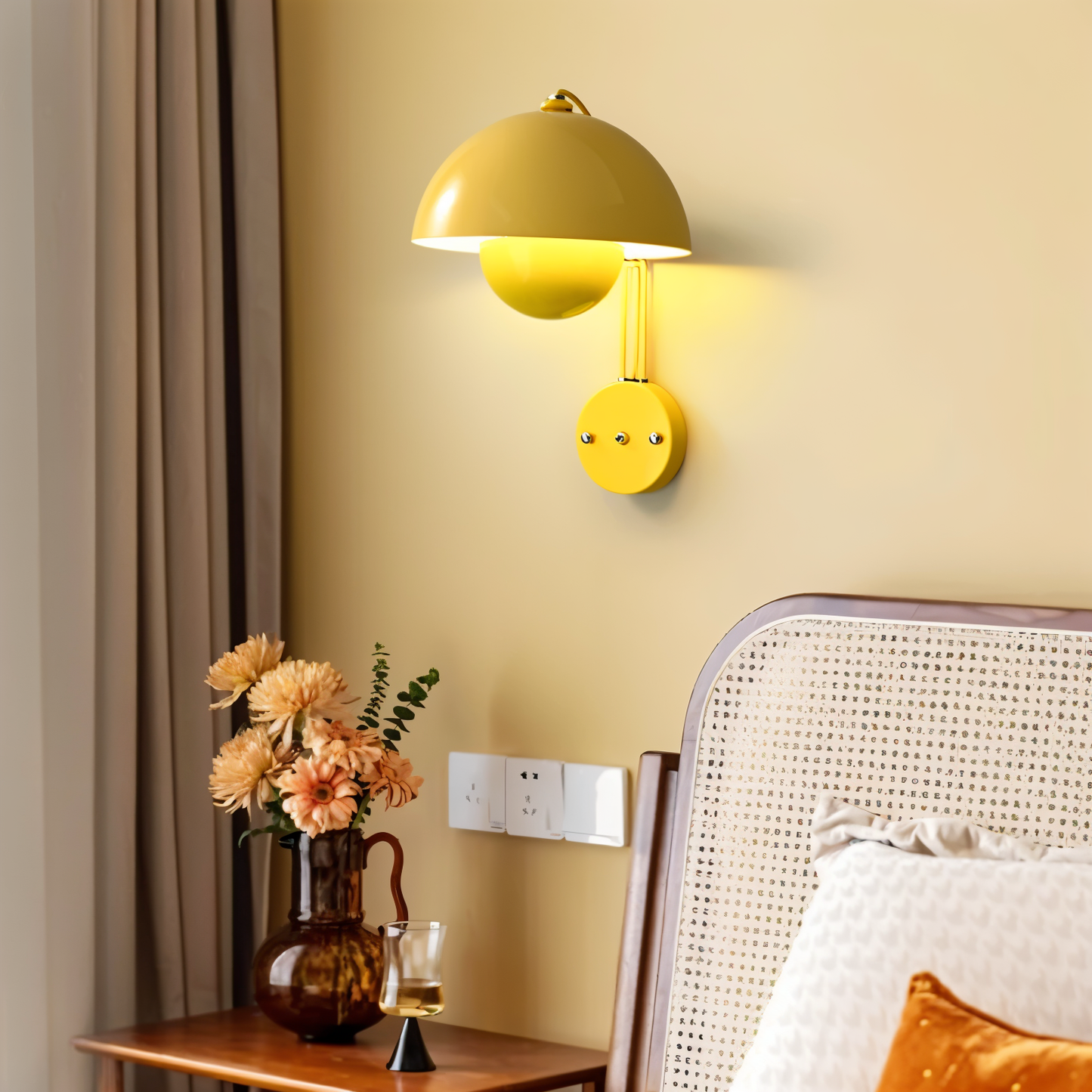 Yellow wall lamp on a beige wall with a vase of flowers and a chair in the foreground.