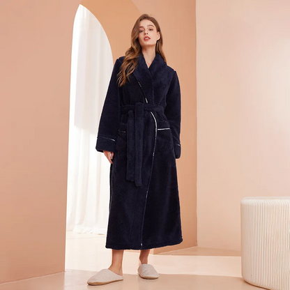 Woman wearing a dark blue robe in a minimalistic room with beige walls and white curtains.