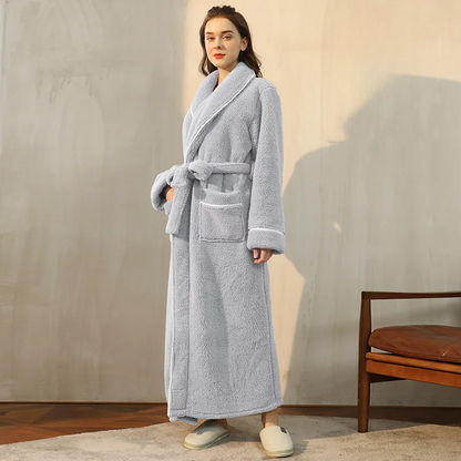 Woman wearing a gray robe standing in a room with a chair and wooden floor.