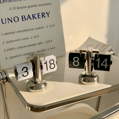 Metallic clock-like objects with numbers on a shelf in front of a UNO BAKERY sign.
