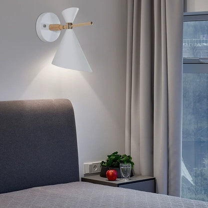 Modern wall lamp on a gray wall above a bed with a nightstand and decorative items.