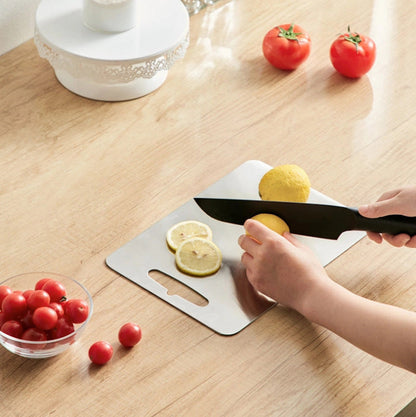 Person slicing lemons on a cutting board with a knife, surrounded by fruits on a wooden table.