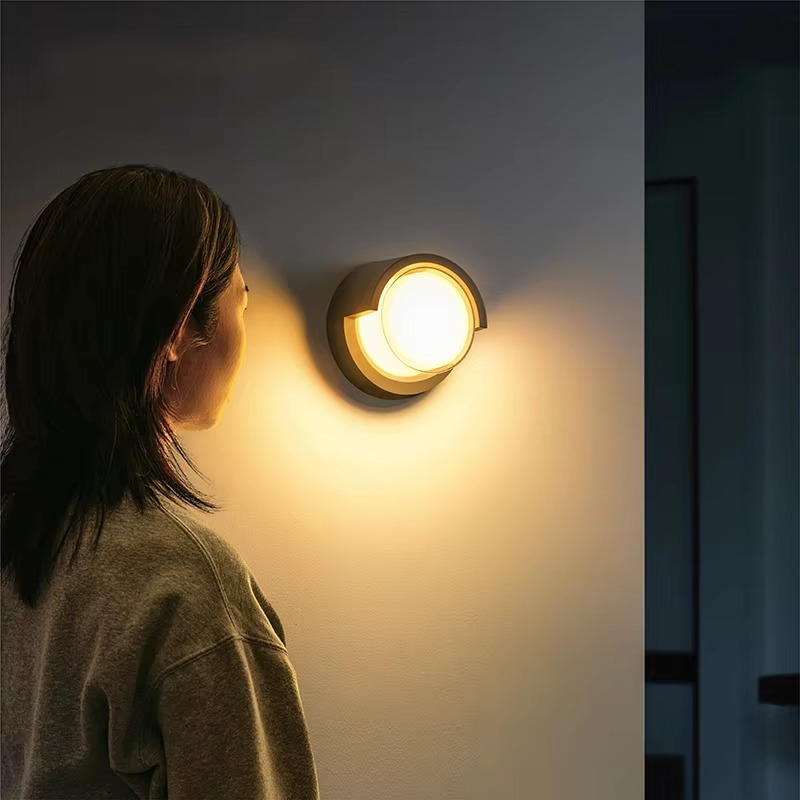 Person standing in a dimly lit room, looking at a wall-mounted light fixture.