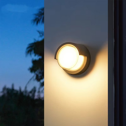 Round outdoor wall light fixture on a building exterior with a blurred natural background