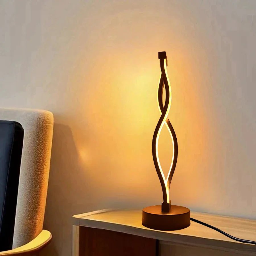 Modern table lamp with a wavy design on a wooden surface, casting a warm glow.