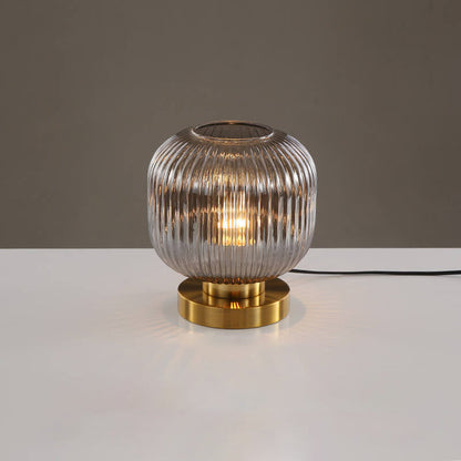 Table lamp with ribbed glass shade and gold base on a white surface with a gray background