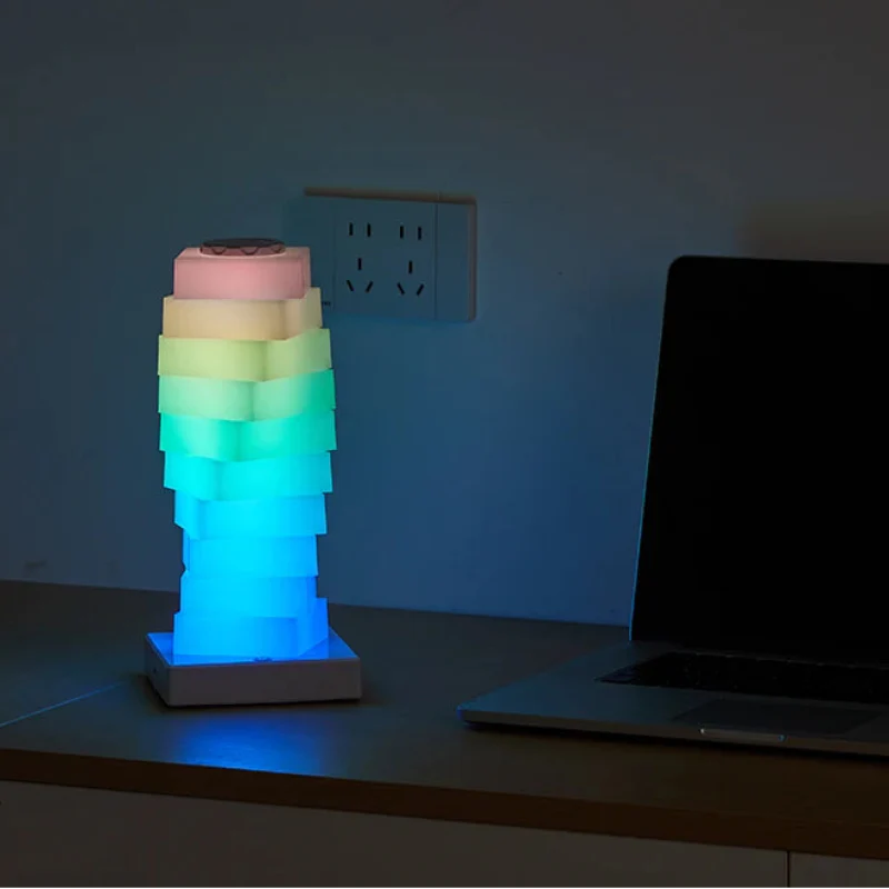 Colorful geometric lamp on a desk with a laptop and headphones in the background