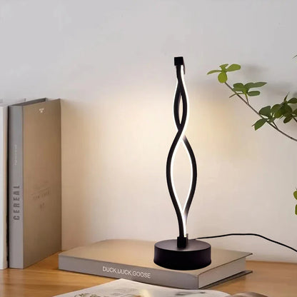 Modern black table lamp on a book with a plant in the background