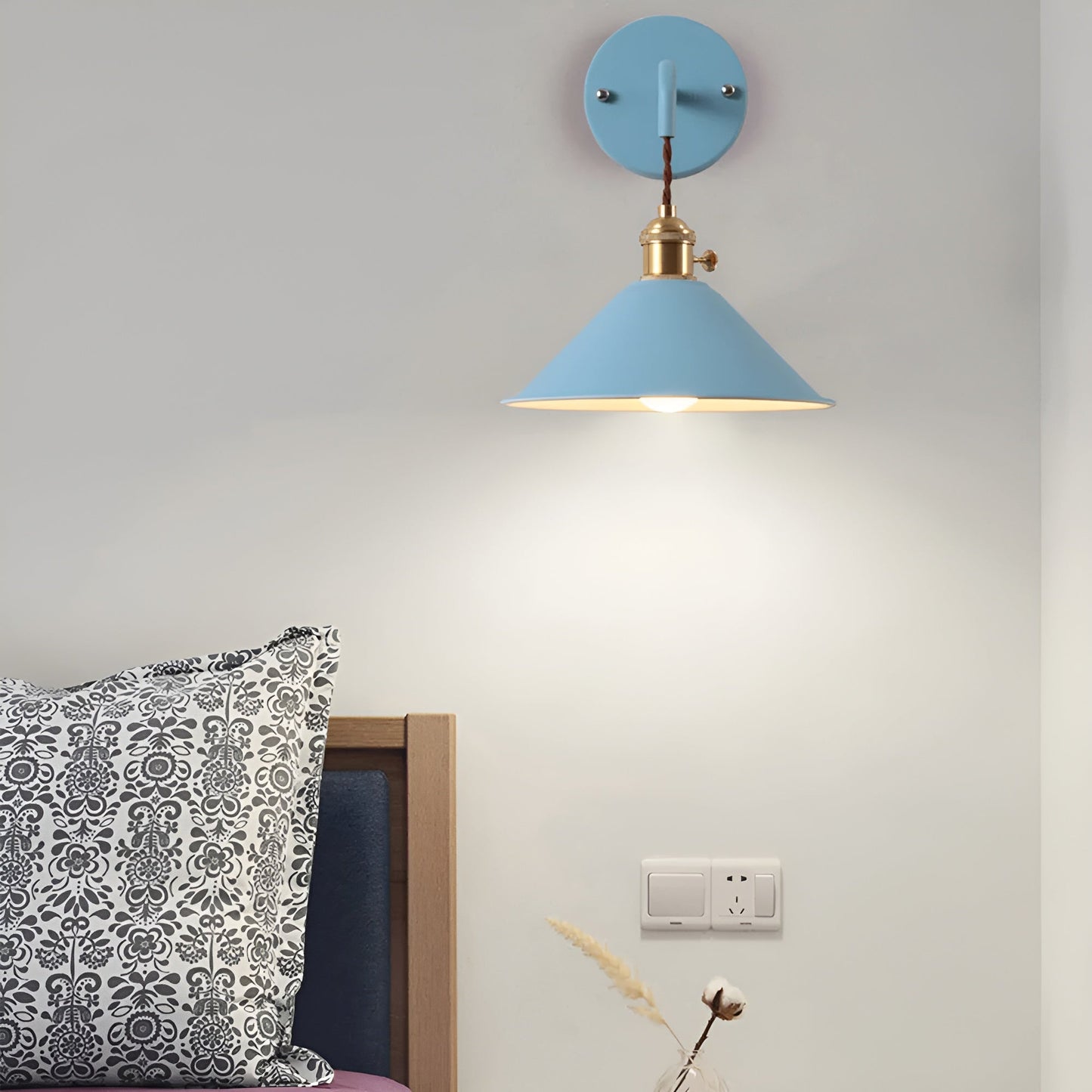 Blue wall lamp on a gray wall with decorative pillow and plant in the foreground