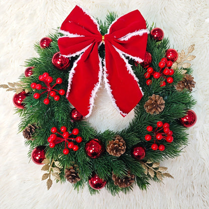 Christmas wreath with red berries, pine cones, and a large red bow on a white background