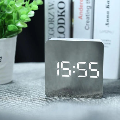 Digital clock displaying time on a table with books and a plant in the background