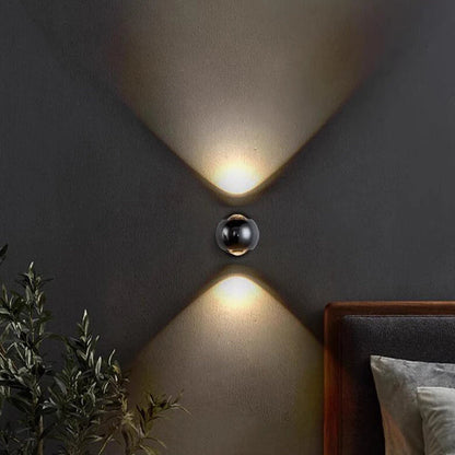 Modern wall lights on a dark wall with a plant and bed in the foreground