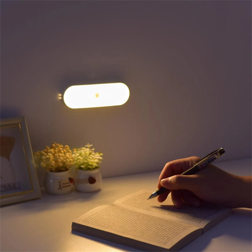 Person writing in a notebook with a pen under a small wall light in a dimly lit room.