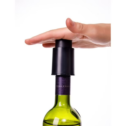 Hand holding a black wine bottle stopper on a green wine bottle against a white background