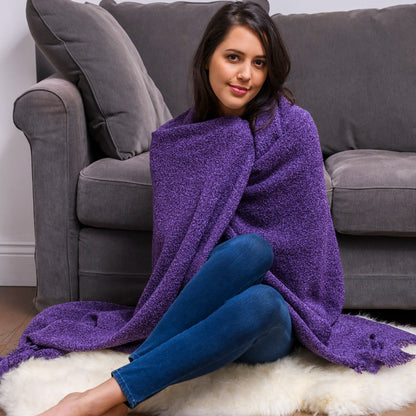 Woman sitting on a rug with a purple blanket wrapped around her, in front of a gray couch.