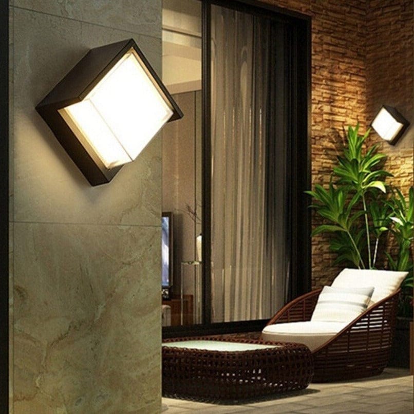 Outdoor wall light fixture on a stone wall with a lounge chair and plants in the background.