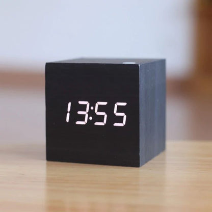 Black digital cube clock on a wooden surface with a blurred background